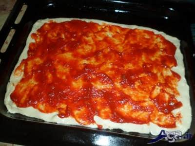 ریختن سس مخصوص پیتزا بر روی خمیر پیتزا 